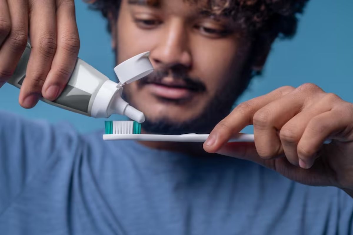 person brushing teeth while applying toothpaste to a toothbrush